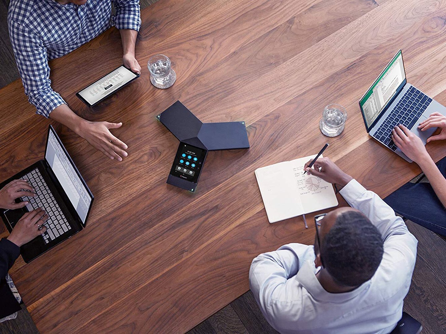 Vier Personen an einem Tisch in einer Sitzung mit einem Telefonkonferenzsystem