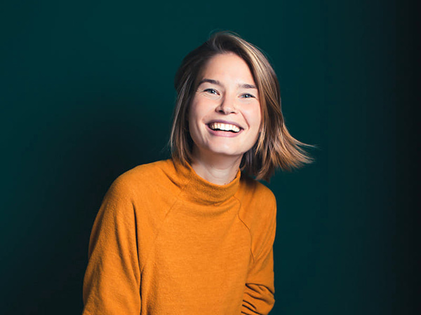 Bild von Carmen Zahno in einem Orangenen Pullover auf grünem Hintergrund